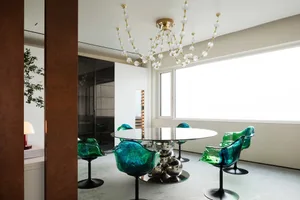Modern dining room featuring round table with metal legs surrounded by green transparent chairs, illuminated by a contemporar