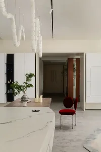 A minimalistic kitchen with marble countertops and a red chair.