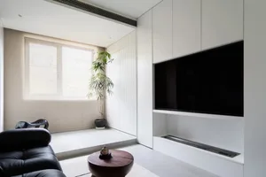 A modern living room with a black sofa, wooden coffee table, and white paneled walls.