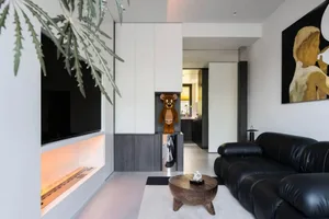 A modern living room featuring a black leather sofa, a wooden coffee table, and an ethereal fireplace with orange lighting, a