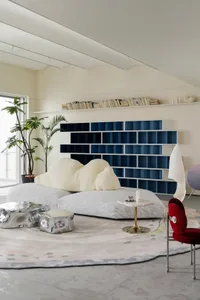 A modern living room featuring plush textiles, metallic furniture, and glass elements.