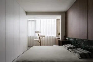 Modern minimalist bedroom featuring light-colored wood walls and floor, a large bed with white and gray bedding, and a white