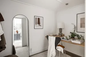 Interior view of a minimalist home office featuring a wooden desk with a leather chair and a white blanket.