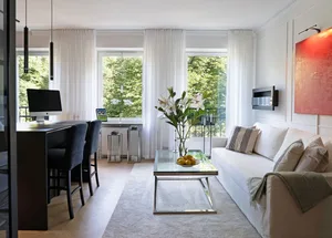 Contemporary minimalist living room with white sofa, glass table, and white curtains.