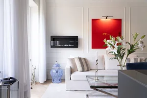 A modern minimalist living room with a white couch, glass coffee table, and red artwork.
