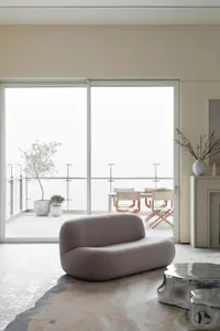 A modern living room with neutral-toned furniture and a large balcony with a dining set.