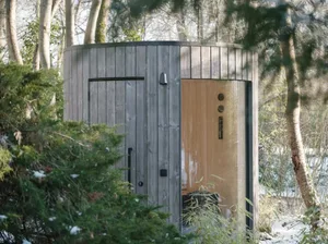 A modern outdoor spa with a wooden exterior surrounded by trees and snow-covered ground.