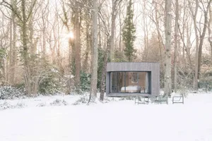 A modern, wooden cabin nestled in a snowy forest, featuring large glass windows and minimalistic design.