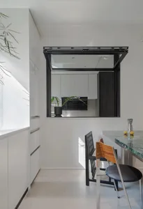 A modern, minimalist kitchen with white cabinets, a white countertop, and a glass window.