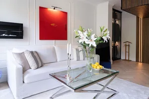 A modern white living room featuring a glass center table adorned with a vase of white lilies and a bowl of lemons.