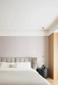 A minimalist bedroom featuring a bed with a fabric headboard against a wall with light gray panels.