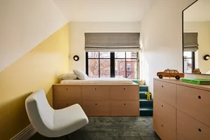 A modern bedroom with a wooden bed frame, white chair, and a window with gray curtains.