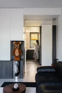 A modern residential interior featuring a black leather sofa and a kitchen entrance.