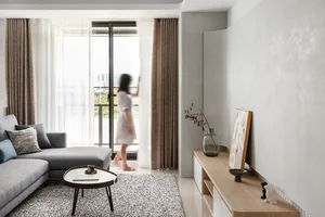 A modern, minimalist living room with a light gray sofa, a round coffee table, and a window with sheer curtains.