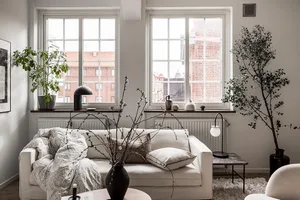 A modern minimalist living room featuring a white couch and a wooden side table with a vase and a plant.