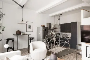 A modern, neutral-toned living room with white walls and floors, featuring a black dining table with matching chairs and whit