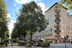 A modern urban building with concrete and glass facade, featuring balconies and retail storefronts.