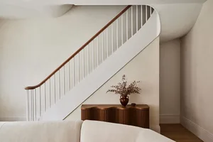 A linear white rail staircase with wooden banisters against a cream-colored wall.