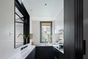 Modern minimalist kitchen with black wooden cabinets, white countertop, and stainless steel appliances.