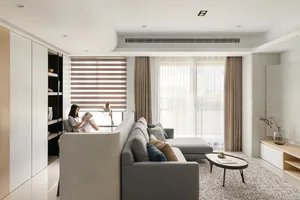 A minimalist living room with fabric curtains, concrete cabinets, and grey sofa, featuring a woman reading a book.