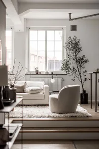 A minimalist white living room with a comfortable sofa, armchair, and plants.