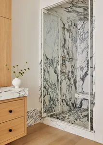 A modern bathroom with a marble shower space featuring a glass door, marble walls, and a wooden vanity.