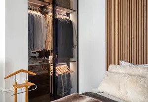 A modern bedroom with a brown wooden wall, built-in closet, and a bed covered in a fluffy blanket.
