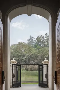An open metal-frame gate overlooking a lush garden with trees and greenery beyond.
