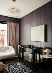 A modern nursery with a black cot, pink furniture, and a chandelier