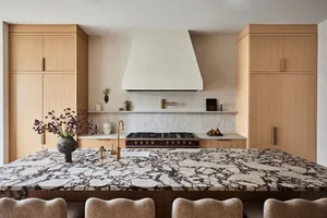 A modern residential kitchen featuring a large marble island with a waterfall edge, wooden cabinets, and a stainless steel ga