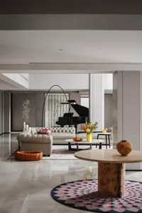 A modern living room featuring marble furniture, including a round table on a colorful patterned rug and a piano in the backg