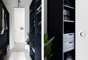A modern closet with black wooden shelves and drawers, featuring a white rug on a wooden floor and a green plant.