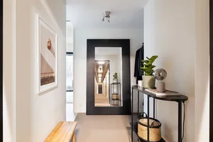 A modern minimalist entrance/hallway showcasing sleek black furnishings and natural light, with a wooden bench and potted pla