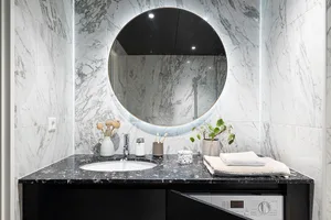 Modern minimalist bathroom with white and black marble counter featuring a round mirror and black countertop.