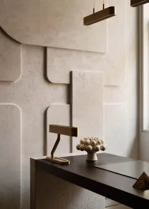A minimalist workspace with a concrete and wood desk, a brass desk lamp, and a decorative sculpture on a textured wall.