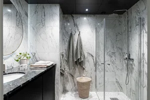 Modern bathroom with marble walls, glass shower enclosure, and black countertop.