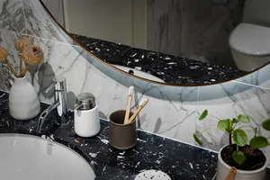 A modern bathroom features a black marble countertop with a sink, faucet, and two toothbrush holders. The background includes