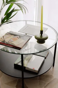 A modern coffee table made of glass and metal with books and a candle.