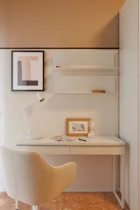 A modern home office setup with a white desk, minimalist shelves, and a beige chair.