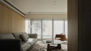 Modern living room featuring a stylish leather couch and wood-paneled walls, with a glass coffee table and vertical blinds.