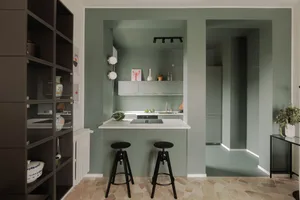 Minimalist kitchen with concrete surfaces, white countertops, and black stools.