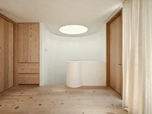 A minimalist bathroom with a white plaster wall and a circular skylight.