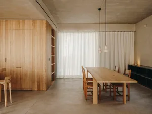 Interior view of a minimalist dining room with wooden furniture and white curtains.