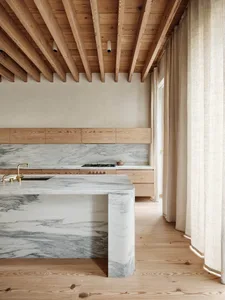 A minimalist kitchen with a marble wooden bar, wooden ceiling beams, and neutral tones.