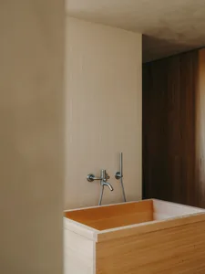 A modern bathroom featuring a wooden bathtub against a white tiled wall and a dark wooden panel.