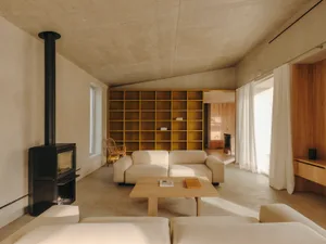 A modern living room with a minimalist design, featuring a concrete ceiling and floor, and a large bookshelf.