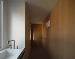 A minimalist bathroom corridor with a white sink and wooden walls.