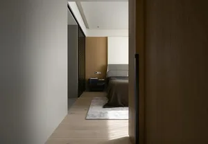 A modern minimalist bedroom with light wood flooring, a white rug, and a grey bed.