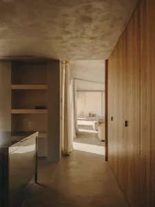 A minimalist living room with concrete walls, wooden paneling, and large windows.