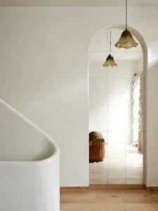 Modern minimalist bathroom with white stone tub and arched mirror.